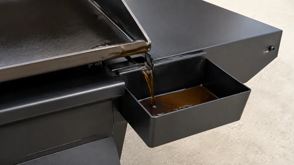 Close-up of the Nexgrill Daytona's side-mounted grease drain cup catching drips at the edge of its cooktop.