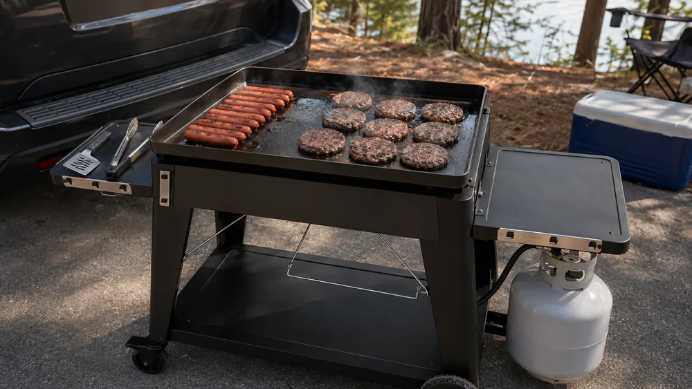 The Pit Boss 4-Burner Fold & Go griddle at a tailgate, hot dogs and burgers cooking across its wide steel top.