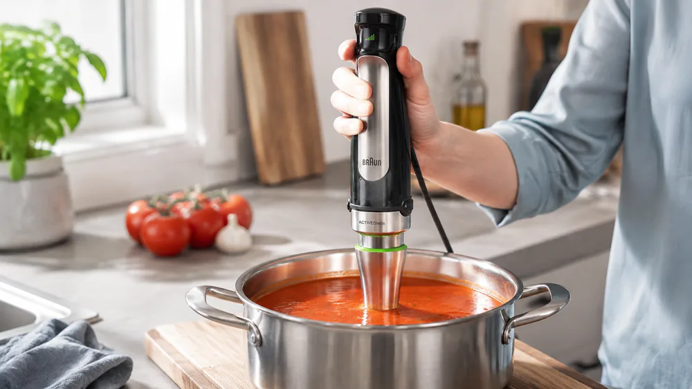 A Braun MultiQuick 7 blending red tomato soup in a stainless steel pot with a clean rim.