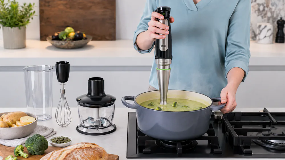 The Braun MultiQuick 7 blending a pot of broccoli-potato soup on a stovetop, steam rising.