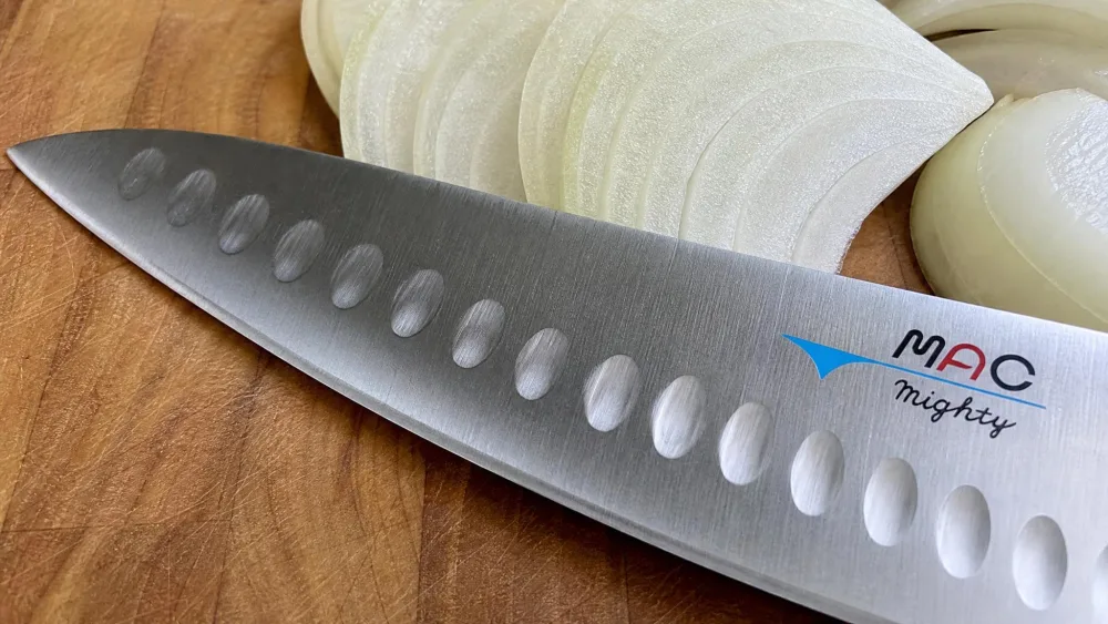 A close-up of the MAC MTH-80 hollow-edge dimples along the blade, with slices of onion on the cutting board.