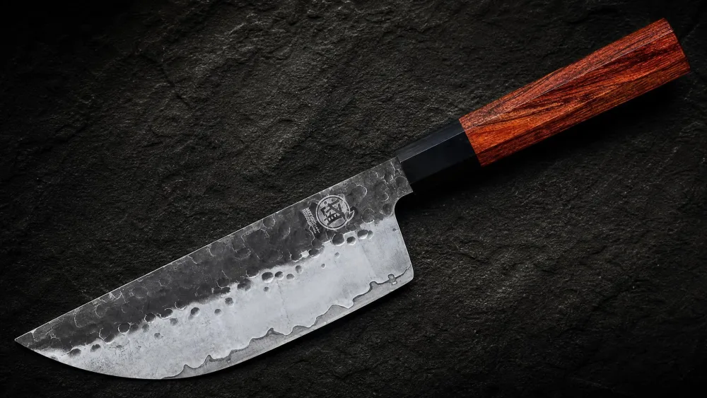 The Mitsumoto Sakari gyuto showing its hammered kurouchi finish beside the rosewood wa handle.