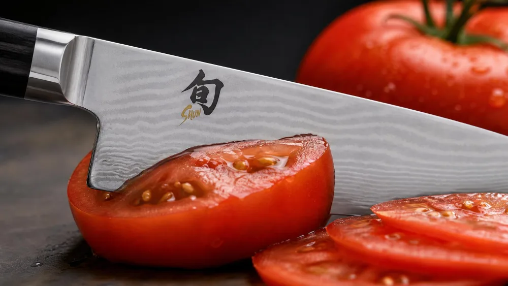 Close-up of the Shun Classic 8-inch edge slicing a ripe tomato, the Damascus pattern visible along the blade.