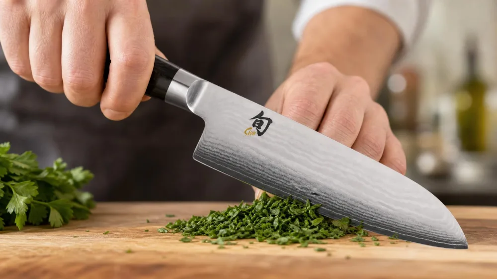 The Shun Classic 7-inch santoku making vertical cuts through herbs on a cutting board.