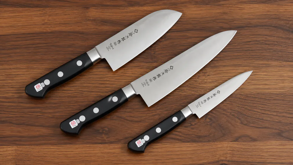 Three Tojiro DP knives in the budget lineup: a santoku, a gyuto, and a petty, laid out on a wooden board.