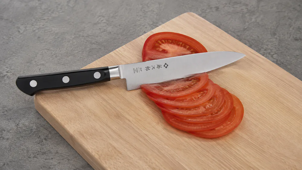 A Tojiro DP petty knife making paper-thin slices of a tomato, fine detail work on a small cutting board.