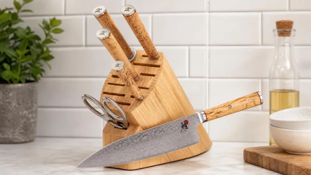 A Miyabi Birchwood GS2 chef's knife with a 101-layer flower Damascus blade pattern and Karelian birch handle resting on a bamboo block.