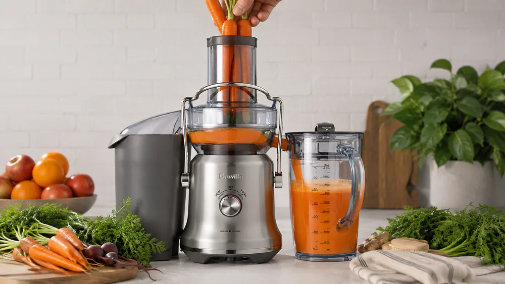 Whole carrots being fed into the 3.5-inch chute of the Breville Juice Fountain Cold Plus while juice fills its 70-ounce jug.