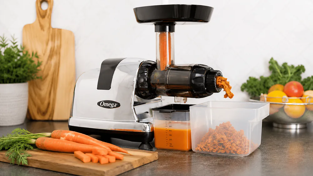 The Omega MM900HDS on a counter with carrots cut for its narrow feed chute and dry pulp ejecting into the pulp bowl.