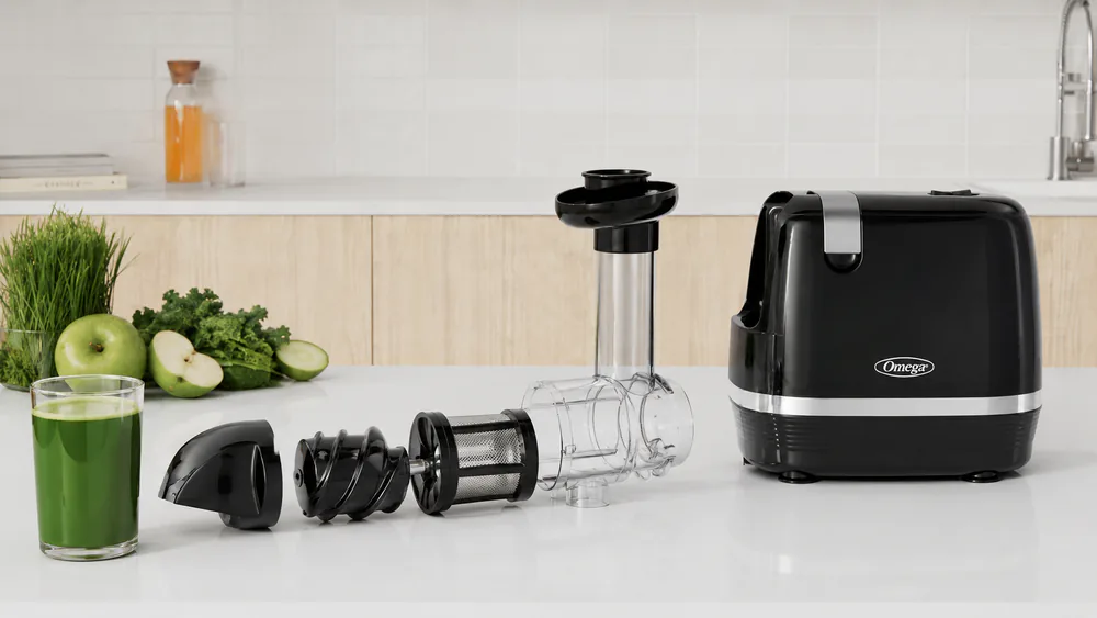 A glass of green juice beside a disassembled Omega H3000D juicer, its parts laid out for a quick rinse.