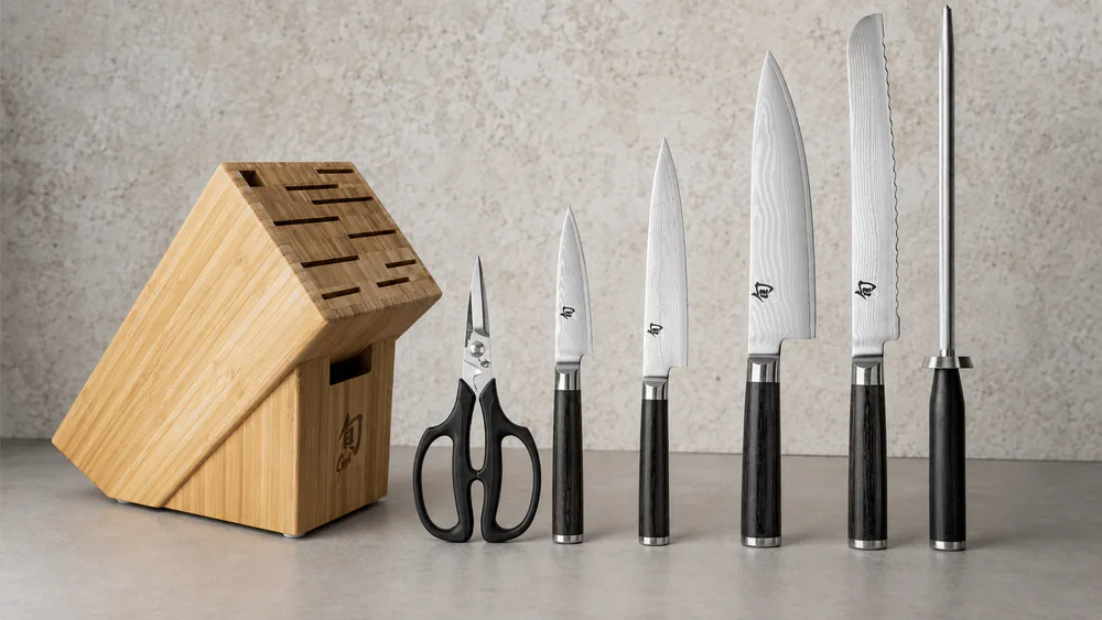 A close-up of the layered Damascus pattern on a Shun Classic chef's knife blade next to a bamboo block on a counter.