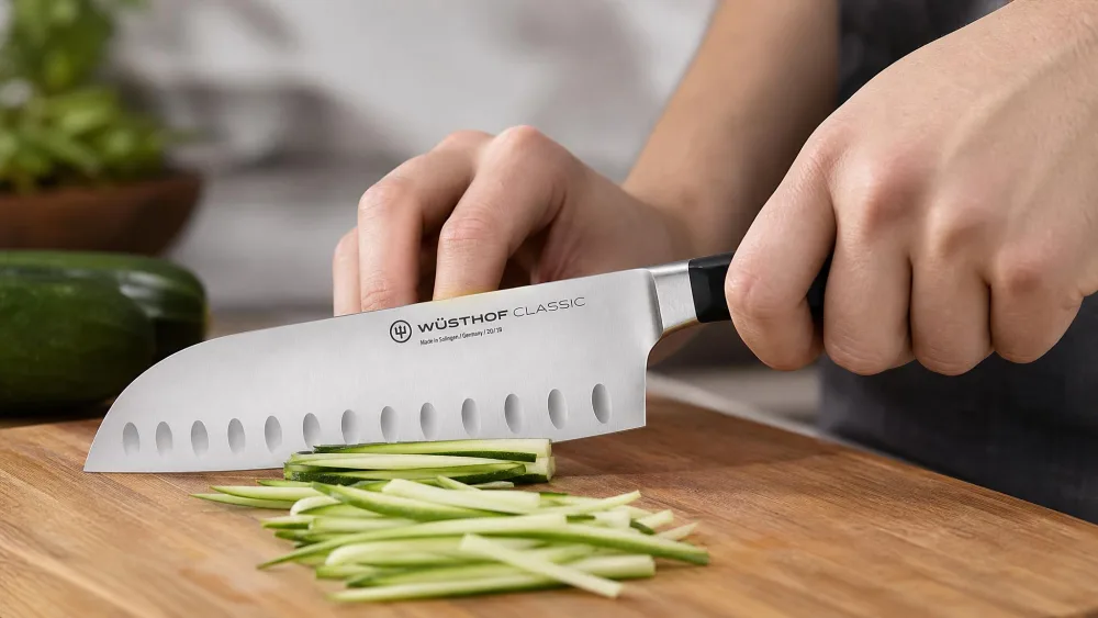 A Wüsthof Classic 7-inch hollow-edge santoku slicing vegetables into thin strips.