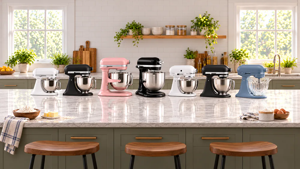Seven KitchenAid stand mixers of different sizes lined up on a kitchen counter with bowls of flour, butter, and eggs in front of them