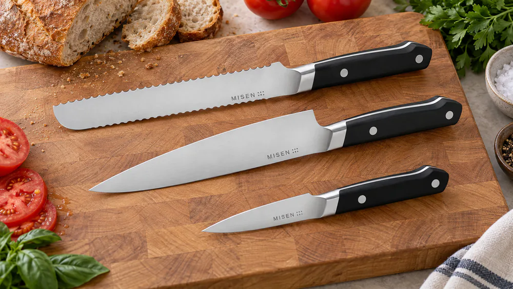The Misen 8-inch chef's knife with its sloped bolster and riveted composite handle, angled to show the thin 15-degree edge.