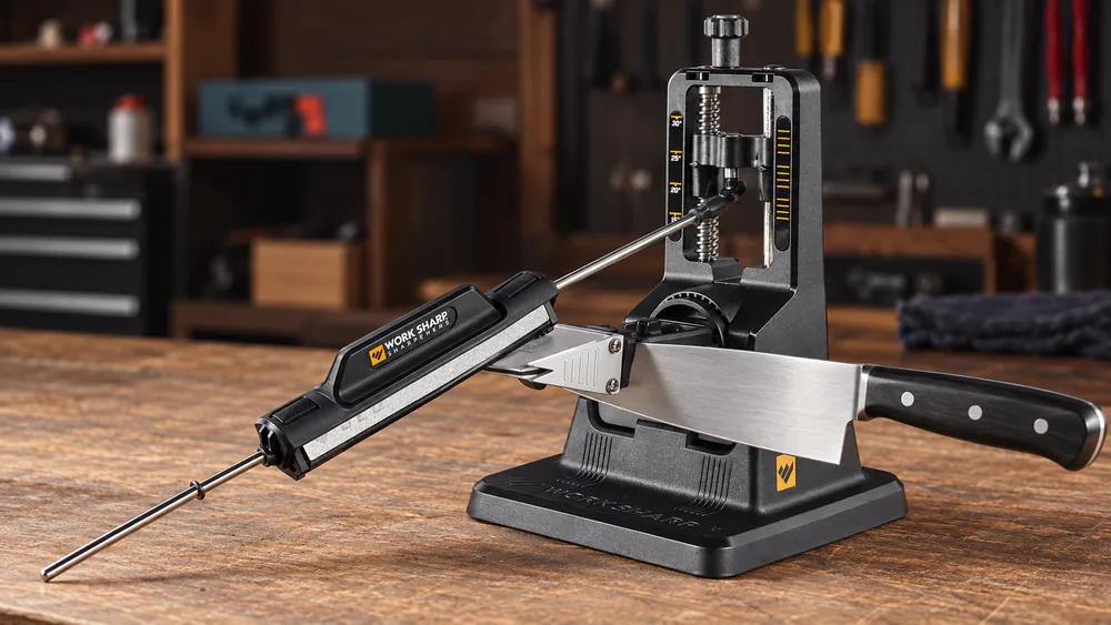 A chef's knife clamped in the Work Sharp Precision Adjust benchtop base, the threaded angle tower visible at the rear.