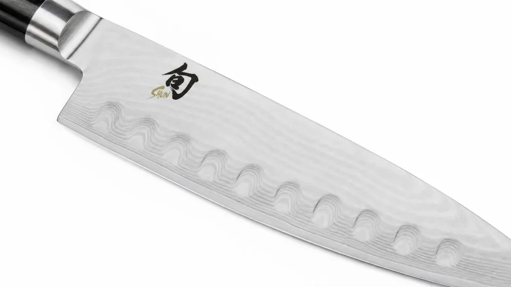 Close-up of the Damascus-clad blade of a Shun Classic 8-inch chef's knife, showing the wavy layered pattern running up from the cutting edge toward the spine.