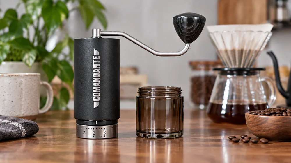 The Comandante C40 MK4 with its etched click dial and dark glass jar beside a pour-over dripper.