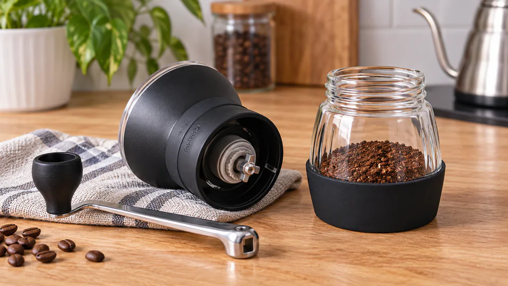 A Hario Skerton Pro over its glass grounds bowl, a batch of medium-coarse grounds inside.