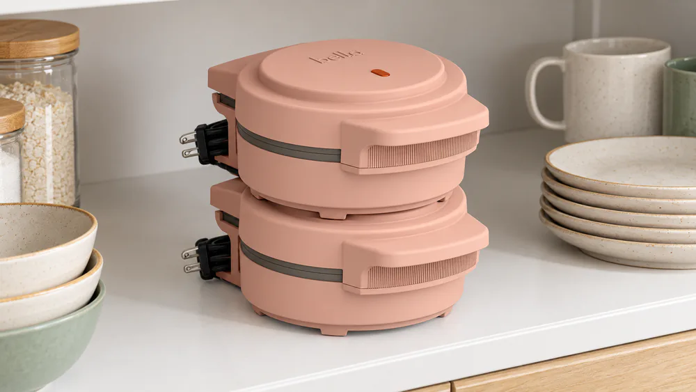 A stackable mini waffle maker with its cord wrapped around the base, sitting on a kitchen shelf