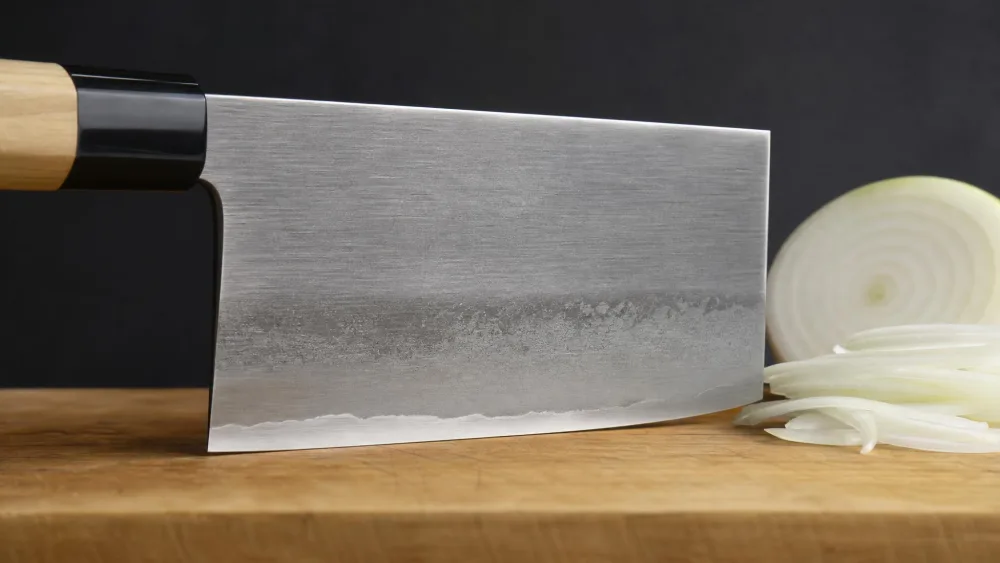 A close-up of a nakiri blade profile showing the flat, tall rectangular shape and square tip beside a sliced onion.