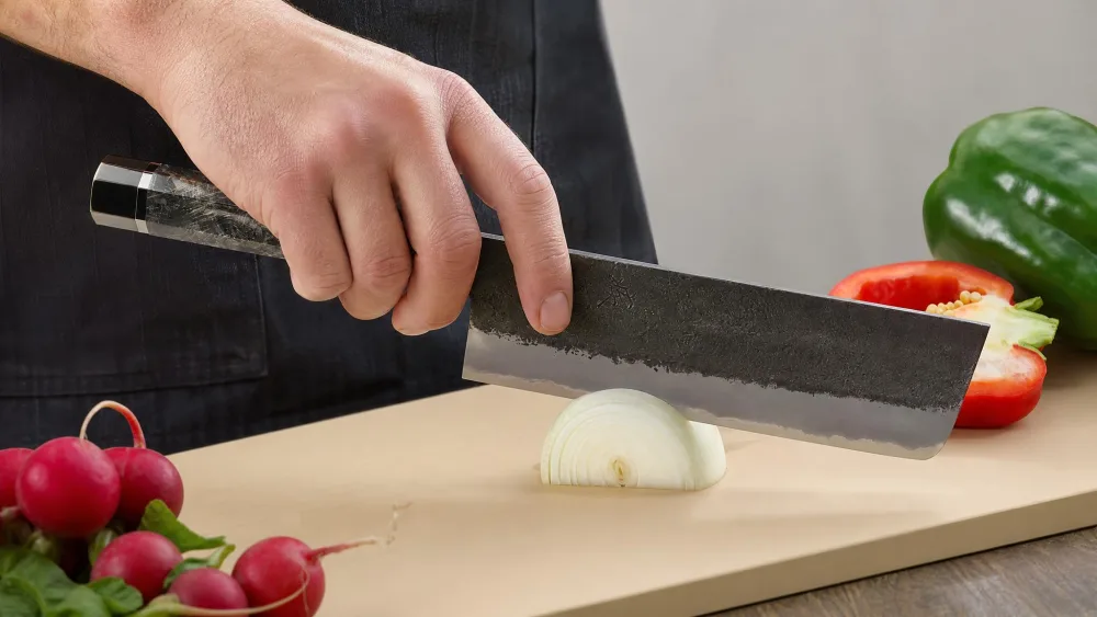 A pinch grip on a nakiri handle with the flat blade vertical, mid push-cut through an onion.