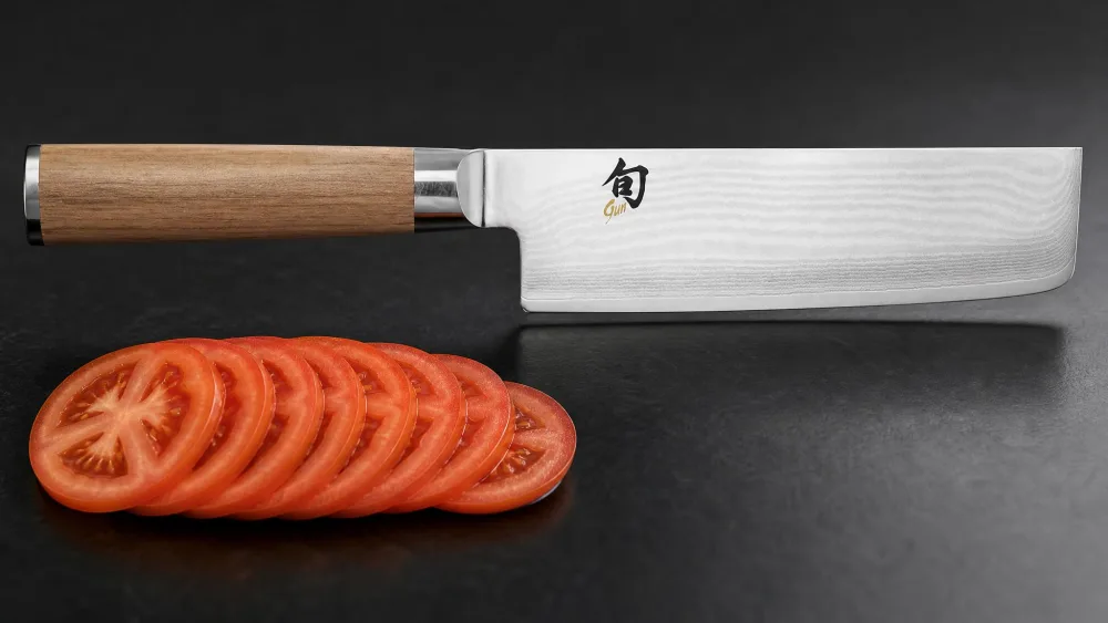 The 68-layer Damascus pattern of the Shun Classic nakiri with paper-thin tomato slices beside it.