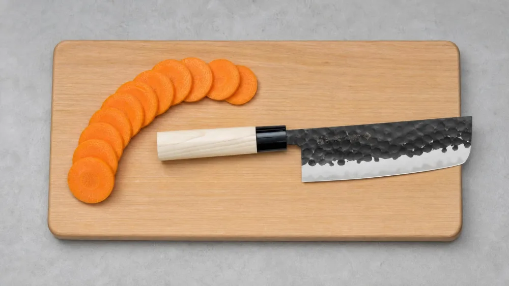 Uniform carrot coins fanned out on a cutting board beside the Tojiro DP nakiri that sliced them.