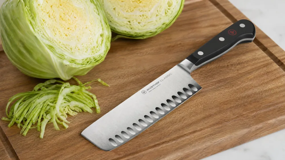 A Wüsthof Classic nakiri on a cutting board, the hollow granton edge dimpling the blade face, beside halved cabbage.