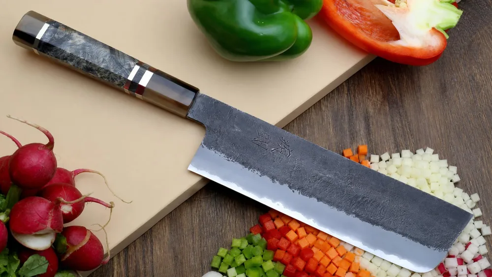 The dark kurouchi finish on the Yoshihiro nakiri blade with a pile of finely diced vegetables beside it.