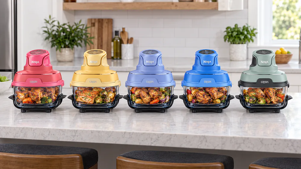 Ninja Crispi glass air fryers in Cherry Crush, Ginger Snap, Frosted Lilac, Electric Cobalt and green Sage lined up on a kitchen counter