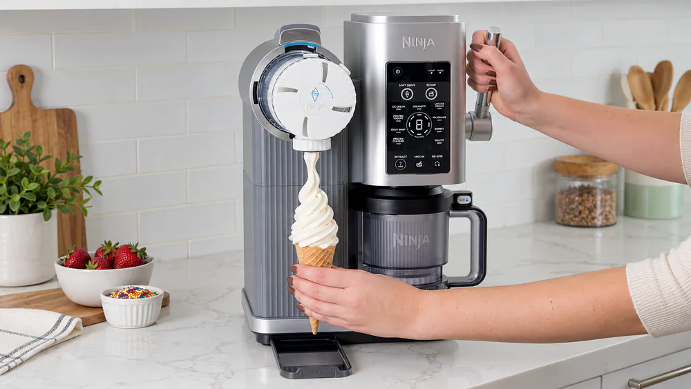 A Ninja Creami Scoop & Swirl NC701 dispensing a tall swirl of vanilla soft serve into a cone through its dispensing lid and handle.