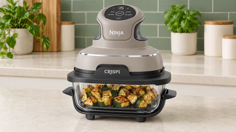 The Ninja Crispi 4-in-1 PowerPod seated on its 4-qt glass container, browned diced zucchini visible through the glass.
