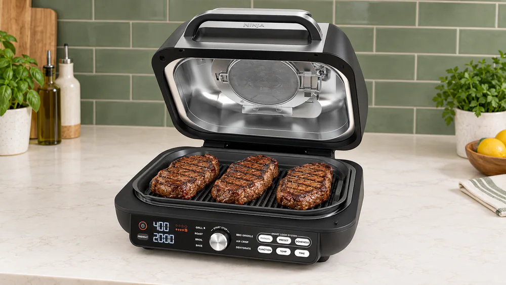 Several steaks with dark edge-to-edge grill marks on the powered grate of a Ninja IG651 with the hood raised
