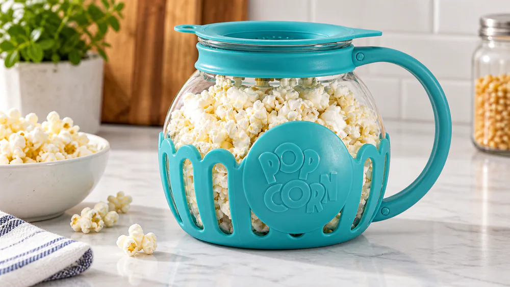 An Ecolution Micro-Pop glass bowl with its measuring lid on a counter, filled with popcorn.