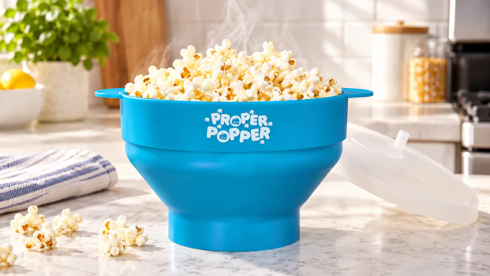 A Proper Popper silicone bowl full of freshly popped popcorn on a counter, handles out, steam rising.