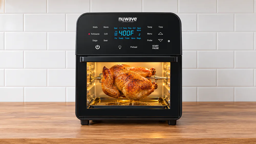Nuwave Brio 15.5-quart oven with a browned whole chicken turning on the rotisserie skewer behind the glass door