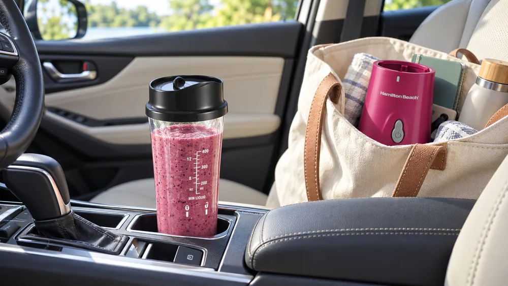 A Hamilton Beach Personal Blender 51131G jar with its travel lid standing in a car cup holder next to the compact 300W base.