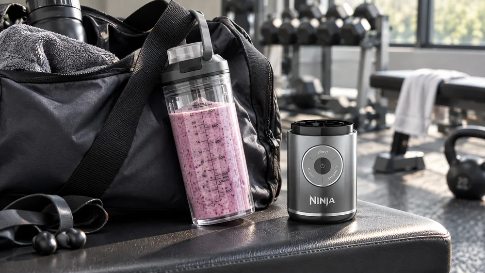 A Ninja Blast Max BC251 with its 22-oz vessel detached from the motor base, the silicone carry handle hooked over the strap of a gym bag.