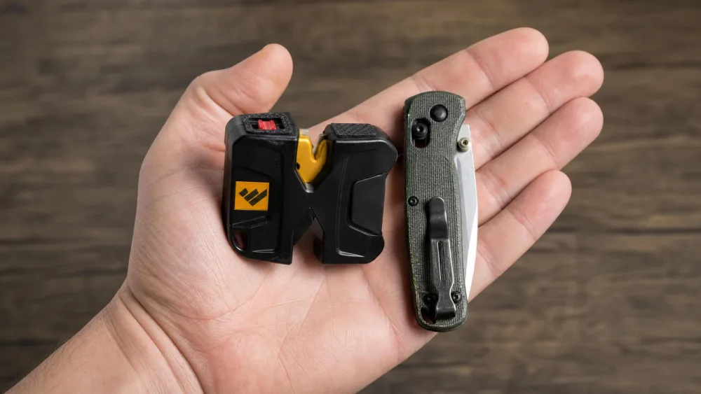 A Work Sharp Pivot in the palm of a hand next to a small folding knife, showing the pocket-sized pull-through sharpener with its lanyard hole.