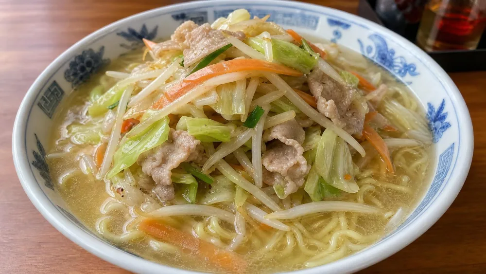 A light salt-broth tan-men ramen heaped with stir-fried cabbage, bean sprouts, carrot ribbons, and thin pork slices over yellow noodles.