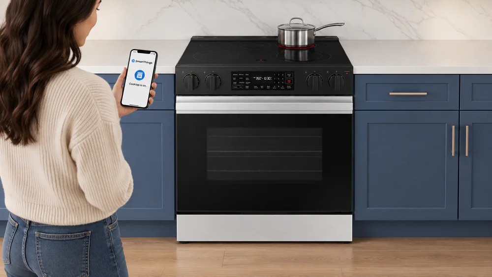A phone showing a SmartThings burner-on notification held in front of a stainless steel Samsung Bespoke slide-in range