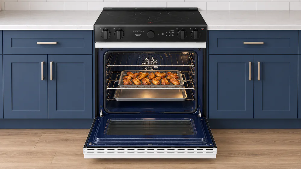 A Samsung air fry tray loaded with crispy chicken wings sitting on the third oven rack above a baking sheet, oven door open