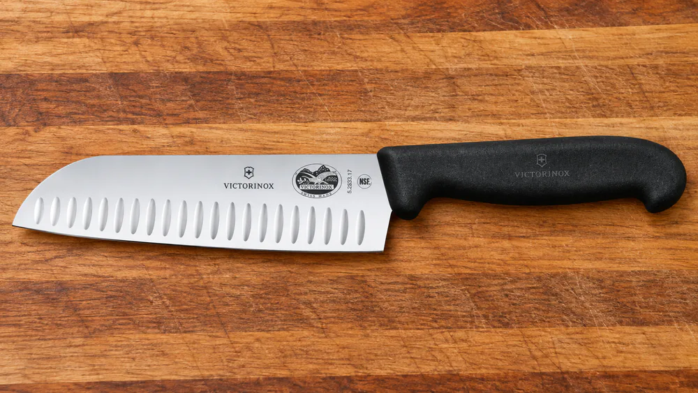 The Victorinox Fibrox 7-inch Granton santoku knife with a fluted blade and black textured Fibrox handle on a cutting board.