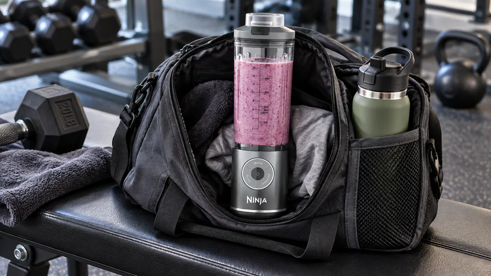 A Ninja Blast Max cordless blender with its 22-oz vessel riding in a gym bag beside a water bottle.