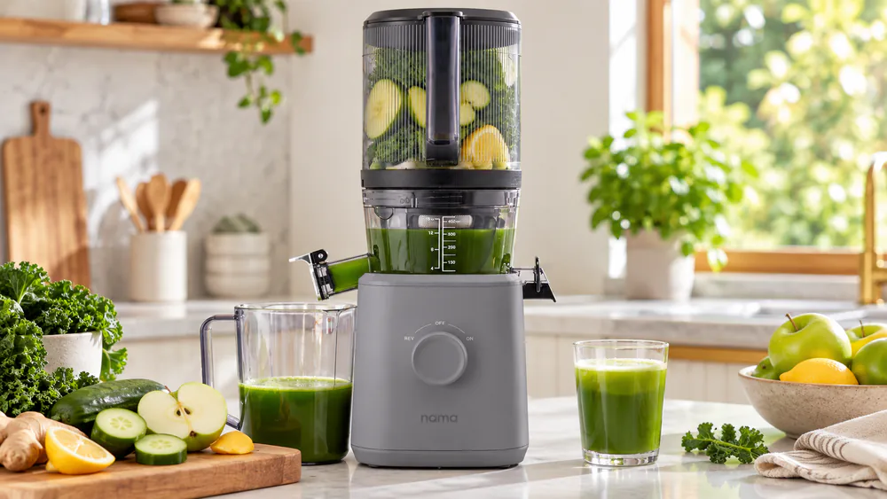 The Nama J2 on a kitchen counter with its hopper loaded with apples and carrots and a full jug of green juice.