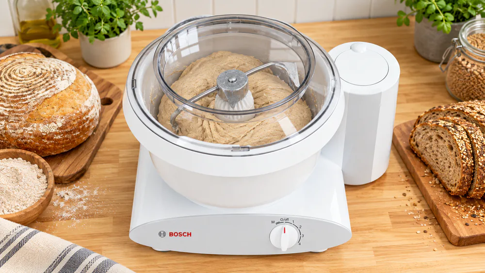 A Bosch Universal Plus bottom-drive mixer with its lid on the 6.5-quart plastic bowl and a dough hook mid-knead