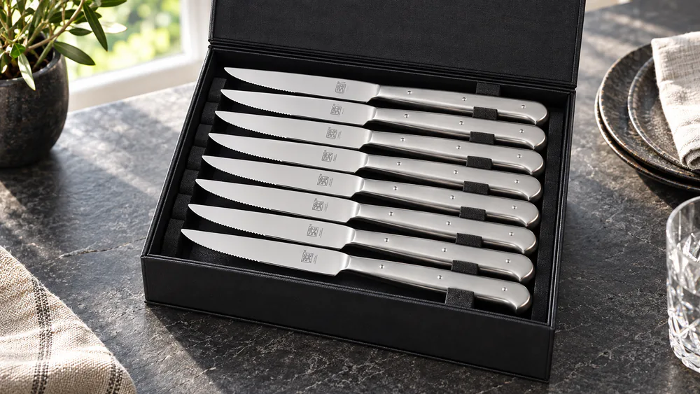A Zwilling Porterhouse set of eight stainless steak knives arranged in a black presentation box that doubles as storage.