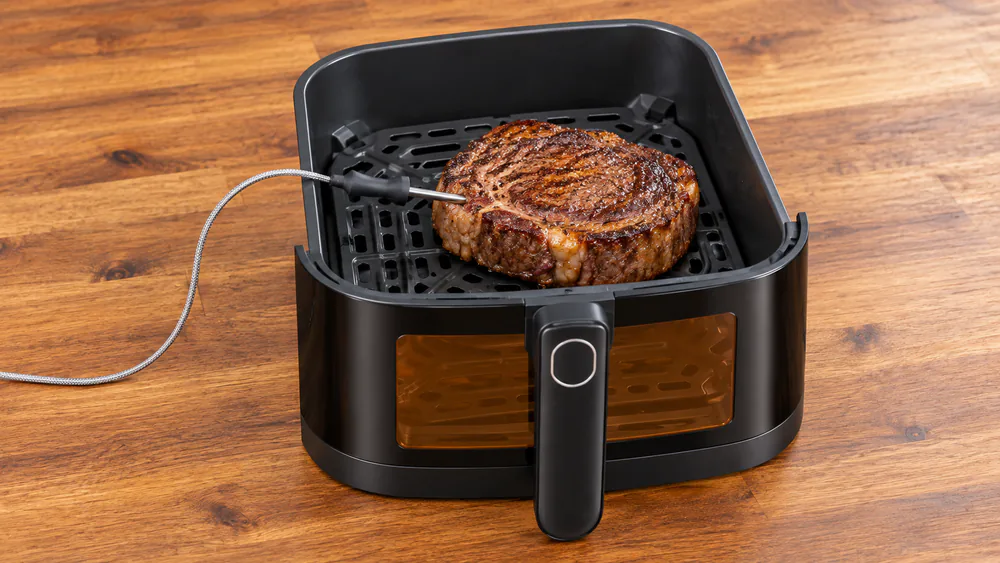 The Tastee Sensor Magic probe inserted into a thick ribeye steak inside the open air fryer basket