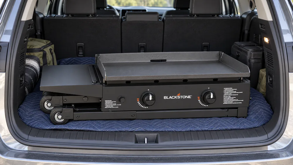 A Blackstone 28-inch griddle with its legs folded and the side shelf down, compact enough to fit in a car trunk or camper for tailgating.