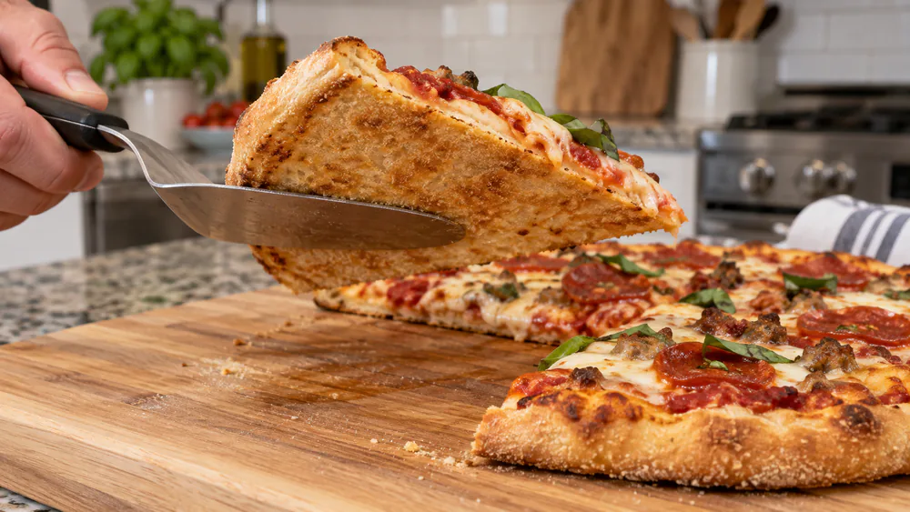 The underside of a homemade pizza baked in the Blackstone E-Series 8013, showing even golden browning from the rotating plate
